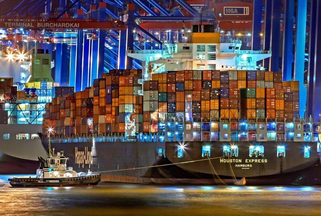 pexels photo 753331 753331 A brightly lit cargo ship at Hamburg harbor with stacked containers and a tugboat.